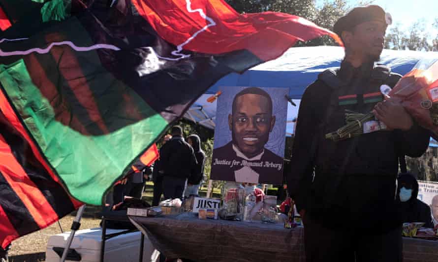 man stands near flags and portrait of Arbery