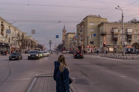 Жена наблюдава движението по широк път с многоетажни сгради от двете страни