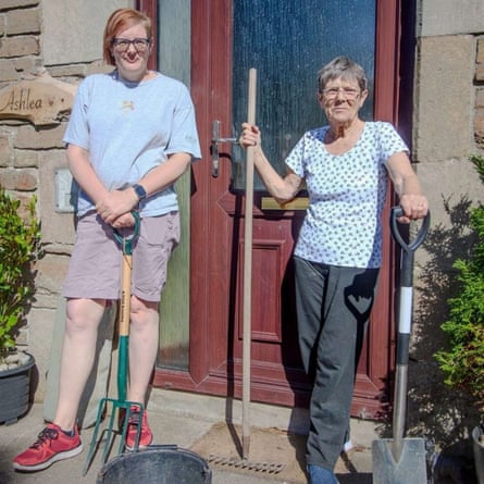 Jen MacDonald and Jenny Paterson stand in front of a front door, holding gardening equipment