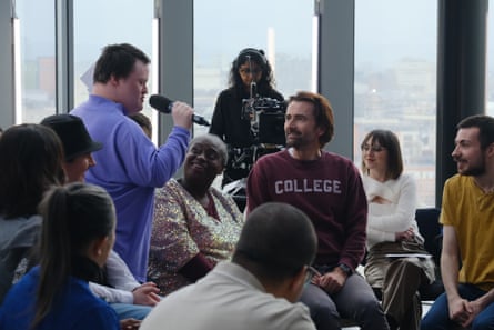 A man with a microphone stands to ask a question of David Tennant who is seated amid the audience