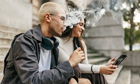 One young man and one young woman sit on university steps as the man vapes