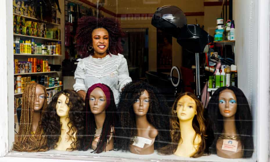 Mariam Campbell of Mayrees hair salon in Aberdeen photographed through the window with dummy heads wearing wigs in front of her