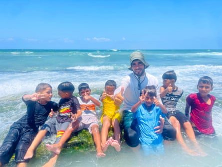 An instructor with a group of the children sitting in the shallows and gesticulating