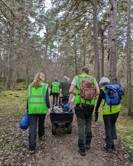 A group of people walking in the woods with a wheelbarrow.