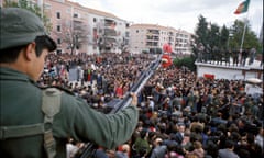 A soldier with a carnation on his rifle in the foreground amid crowds of people in the street below him