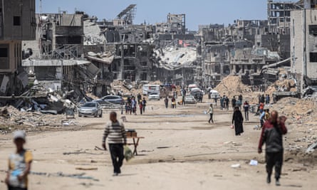 Palestinians walk on deserted street with destroyed building in the background 