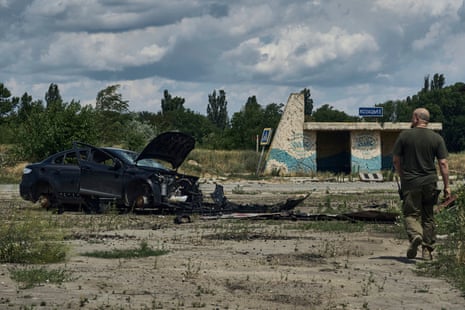 A man passes by a damaged car after Russian shelling in the village of Kozatske.