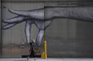 A woman in a mask walks past a mural of a hand on the side of a building in New York. The photo was taken on 22 April, during the citywide coronavirus lockdown