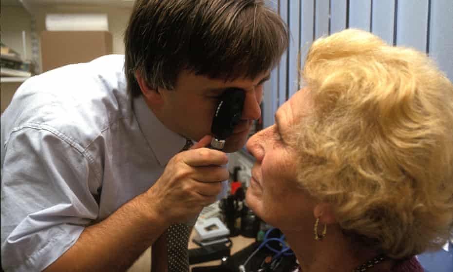 Male GP checking female patients eyes.
