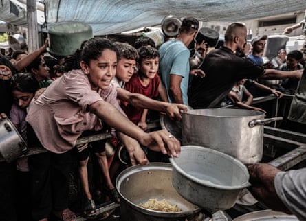 Palestinian children reach out for food with empty pans in Gaza