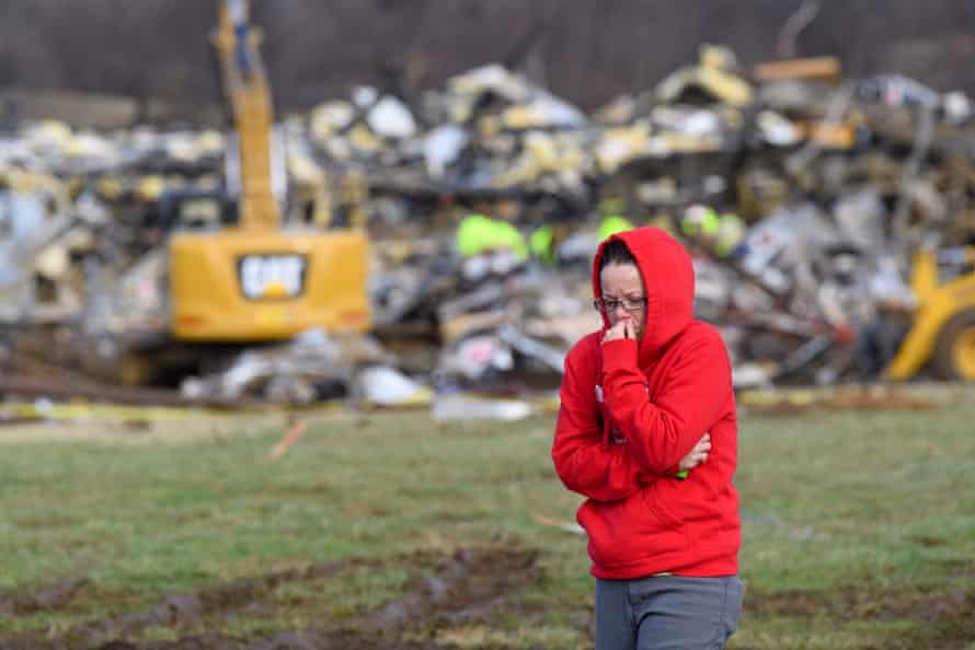 A woman in a red hoodie walks away from the rubble of a candle factory left after a deadly tornado.