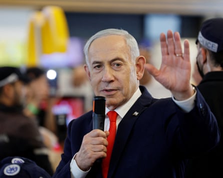Benjamin Netanyahu holds a microphone and raises his hand while speaking