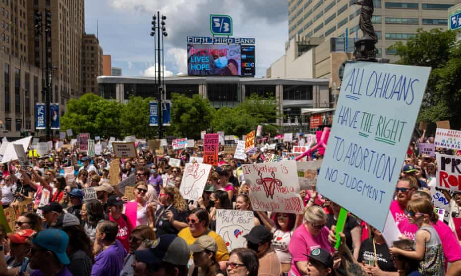 A protest in Ohio where a large crowd holds signs against abortion restrictions. The sign closest reads 'All Ohioans have the right to abortion. No judgment'.