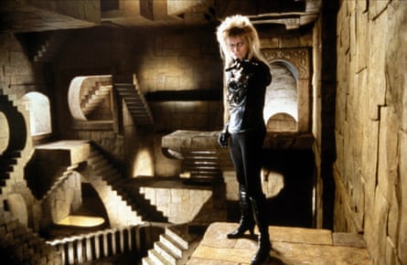 A man with a blond mullet and clad in black leather points at the camera.