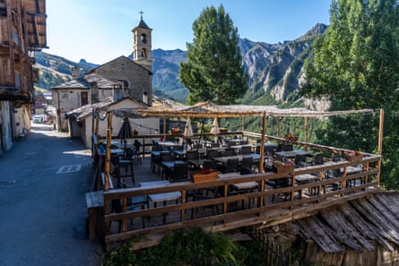 Restaurant outdoor seating with small church and mountains in the background, Saint-Véran