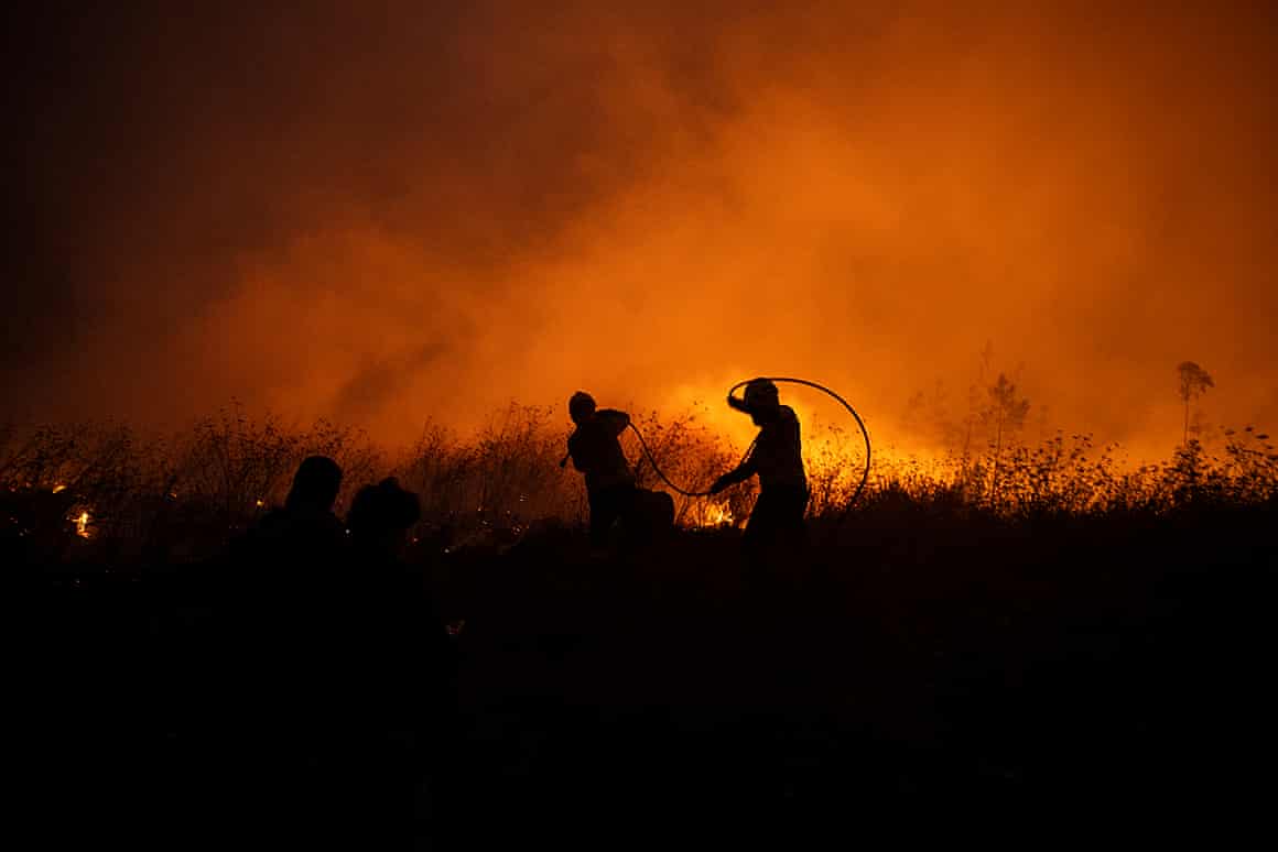 Two firefighters silhouetted against orange smoke and flames