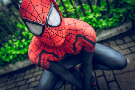 Cosplayer dressed as Spider-Man, sitting down on their haunches and looking into the camera