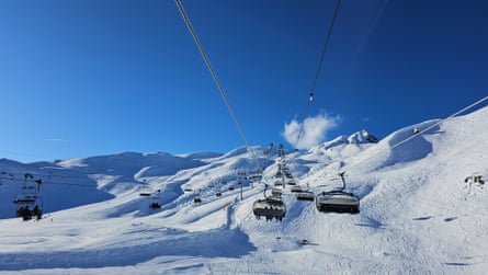 A sunny, snowy mountaintop landscape with ski lifts