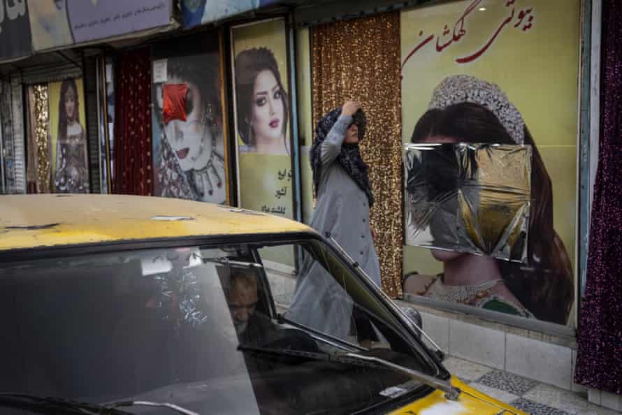 A woman walks in front of beauty salons with defaced window decorations in Kabul, Afghanistan