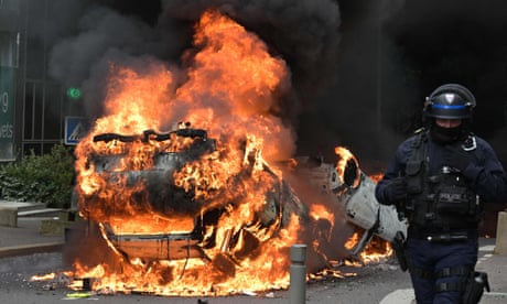 A police officer walks past a burning car in Nanterre at the end of a commemoration march on Thursday for the teenager shot dead by police