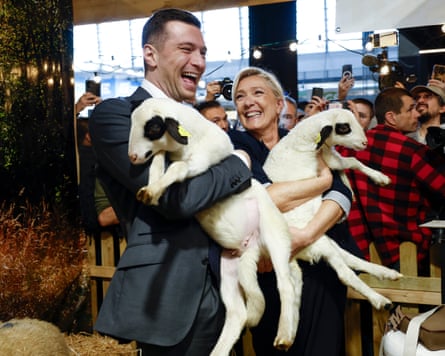 Marine Le Pen and Jordan Bardella hold lambs in their arms at an agricultural show. Both are laughing.