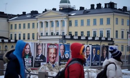 People walk by election posters in Helsinki with the presidential palace in the background