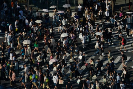 People carry umbrellas to shield themselves from the sun as they walk across an intersection in Tokyo.