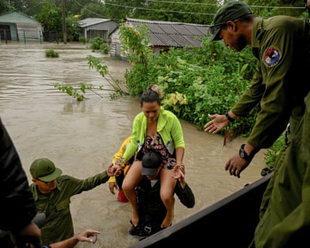 A woman is carried on an army officer’s shoulders across a flooded road to a vehicle where other officers wait to help