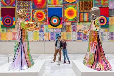 Very colourful images on the wall and huge colourful models of people, with visitors looking at them.