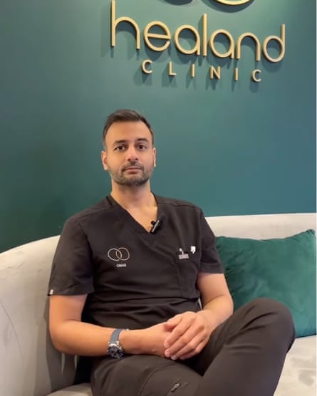 Man in dark clothes similar to surgical scrubs with the Healand clinic logo on the wall behind