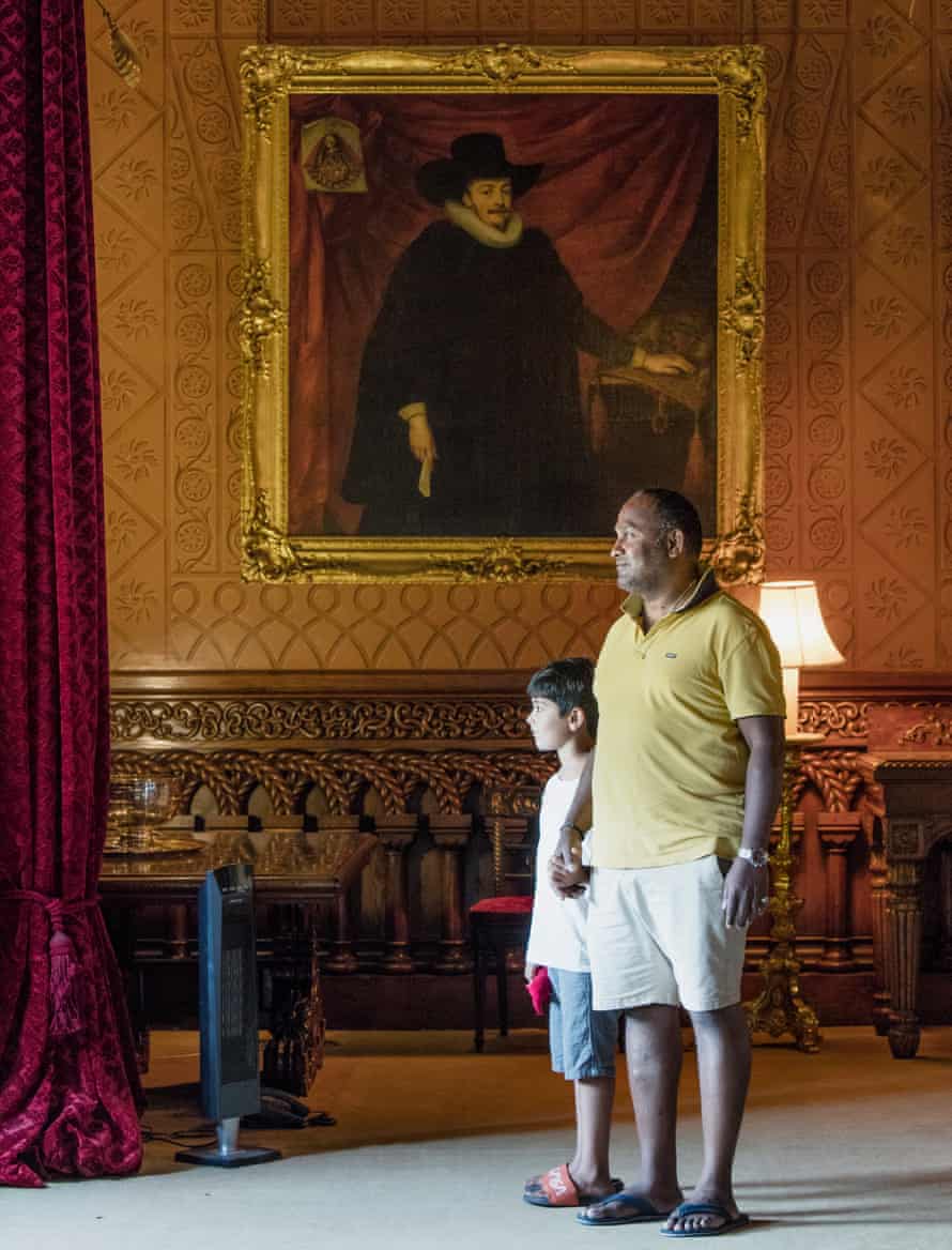 Visitors looking out of the window in Penrhyn Castle’s Dining Room, in front of a portrait of John Williams, from the circle of Marcus Geeraerts