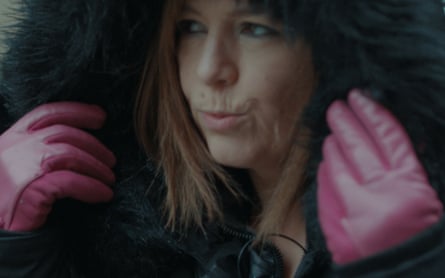 A woman pulls a large black hood up with satin pink gloves on