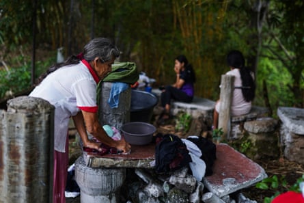 An older woman stands by a pile of broken masonry, using a flat piece of stone as a scrubbing board for clothes.