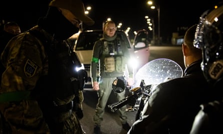 The paramilitaries question a motorcycle driver and his passenger driving after curfew.
