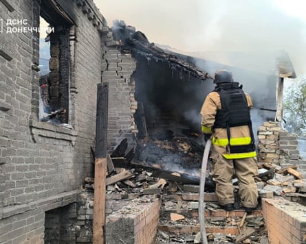A firefighter sprays a hose at a charred and damaged house