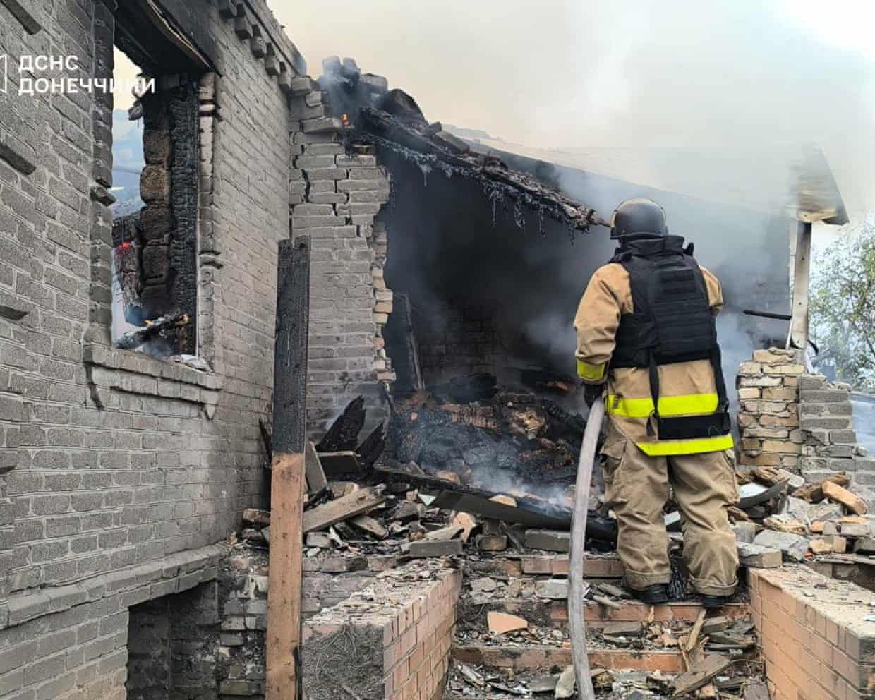 A firefighter sprays a hose at a charred and damaged house