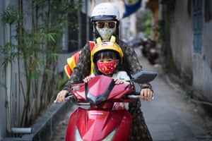 An adult and a child on a red motorbike both wearing facemasks.