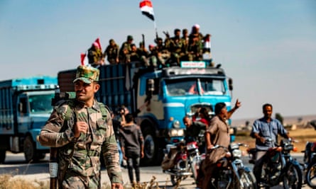 A Syrian government soldier with rifle on soldier in the foreground, with a truck full of troops and a motorcycle escort behind.