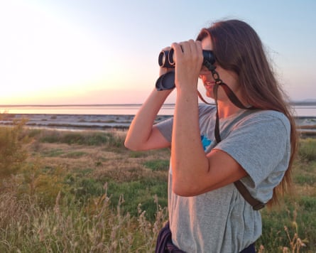 Woman standing by wetlands looking through binoculars