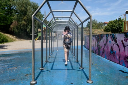 Megan walks through an outdoor walkway that is spraying a mist of water on her in a city park with a wall to one side covered in graffiti.