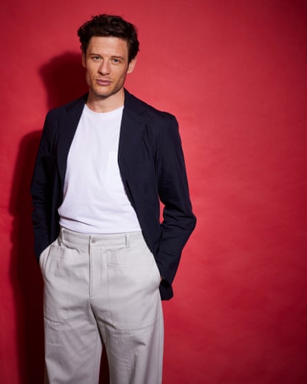 James Norton casually dressed in a jacket, T-shirt and chinos against a red background