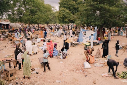 People milling about in an open space with a few selling small piles of goods
