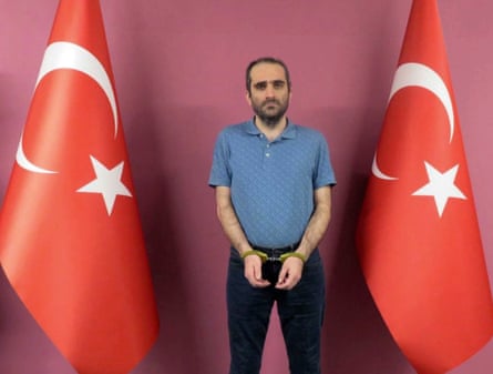 Selahaddin Gülen in handcuffs standing between two Turkish flags