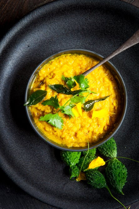 Overhead shot of yellow dal in a black bowl, garnished with coriander and curry leaves