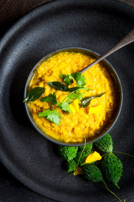 Overhead shot of yellow dal in a black bowl, garnished with coriander and curry leaves