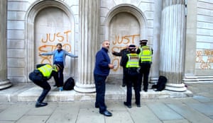 three police officers and two protesters in front of the sprayed words Just Stop Oil