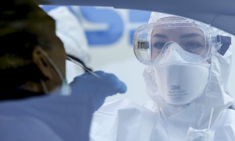 A medical worker wearing protective equipment and mask collects a mouth and nose swab from a person sitting inside a car during a drive-through coronavirus (Covid-19) test in Rome.