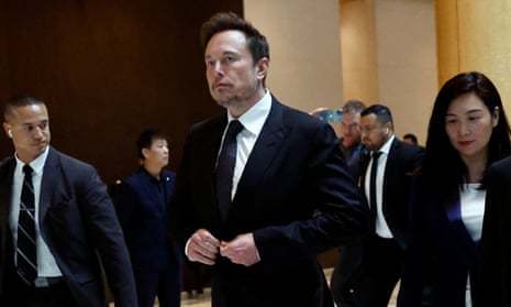 Elon Musk, wearing a suit and tie, leaves a hotel with an entourage