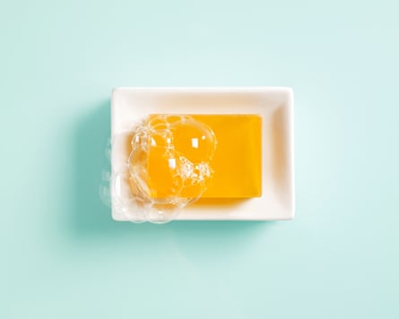 Orange bar of soap in a white ceramic dish on a light green background