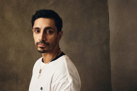 A head and shoulders portrait shot of Riz Ahmed, standing side on to the camera, wearing a cream top